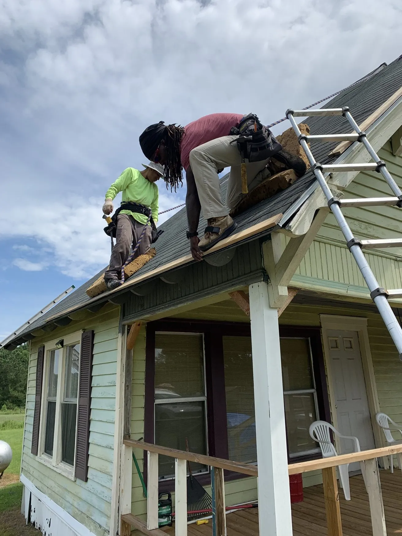 Two roofers fastening new shingles along the edge of a roof